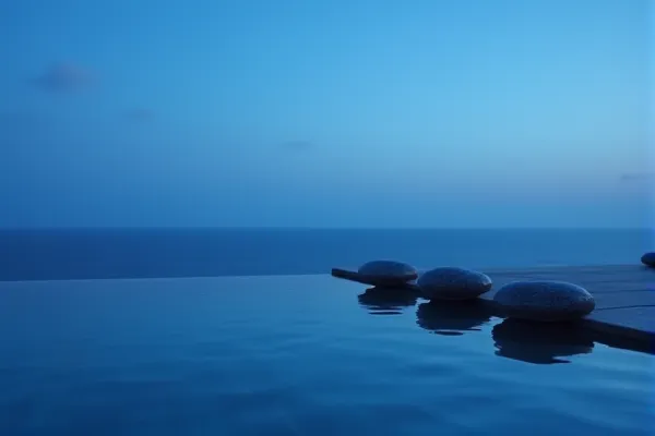 Three dark, smooth elements stand in absolute alignment beside a surface of liquid equilibrium under the quiet glow of evening.